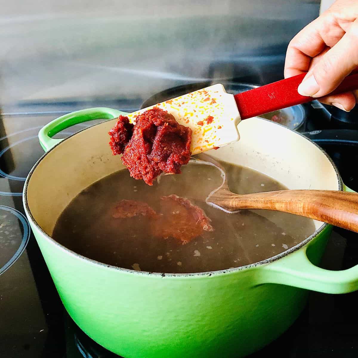 Adding ginger/garlic/tomato paste to a large pot containing cooking black urad bean daal