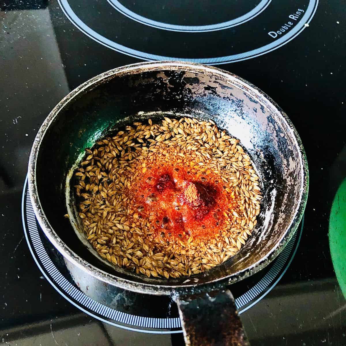 A small frying pan containing cumin seeds, Asafoetida and chilli powder frying in hot oil.