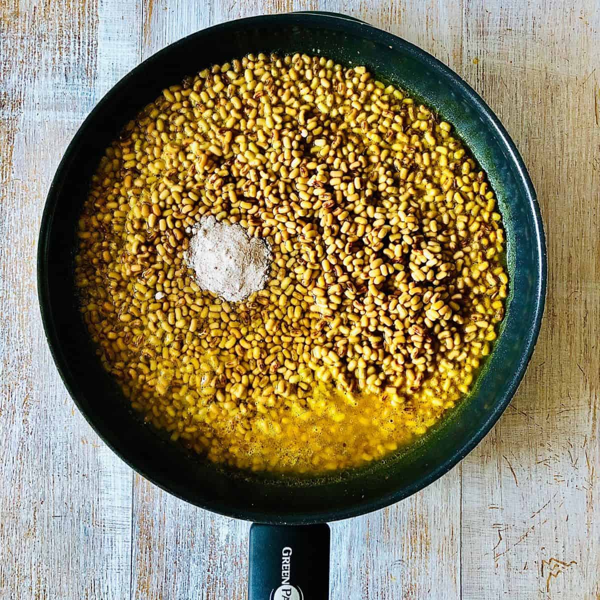 A large frying pan containing cooked moth daal ingredients with salt added, ready to mix in.
