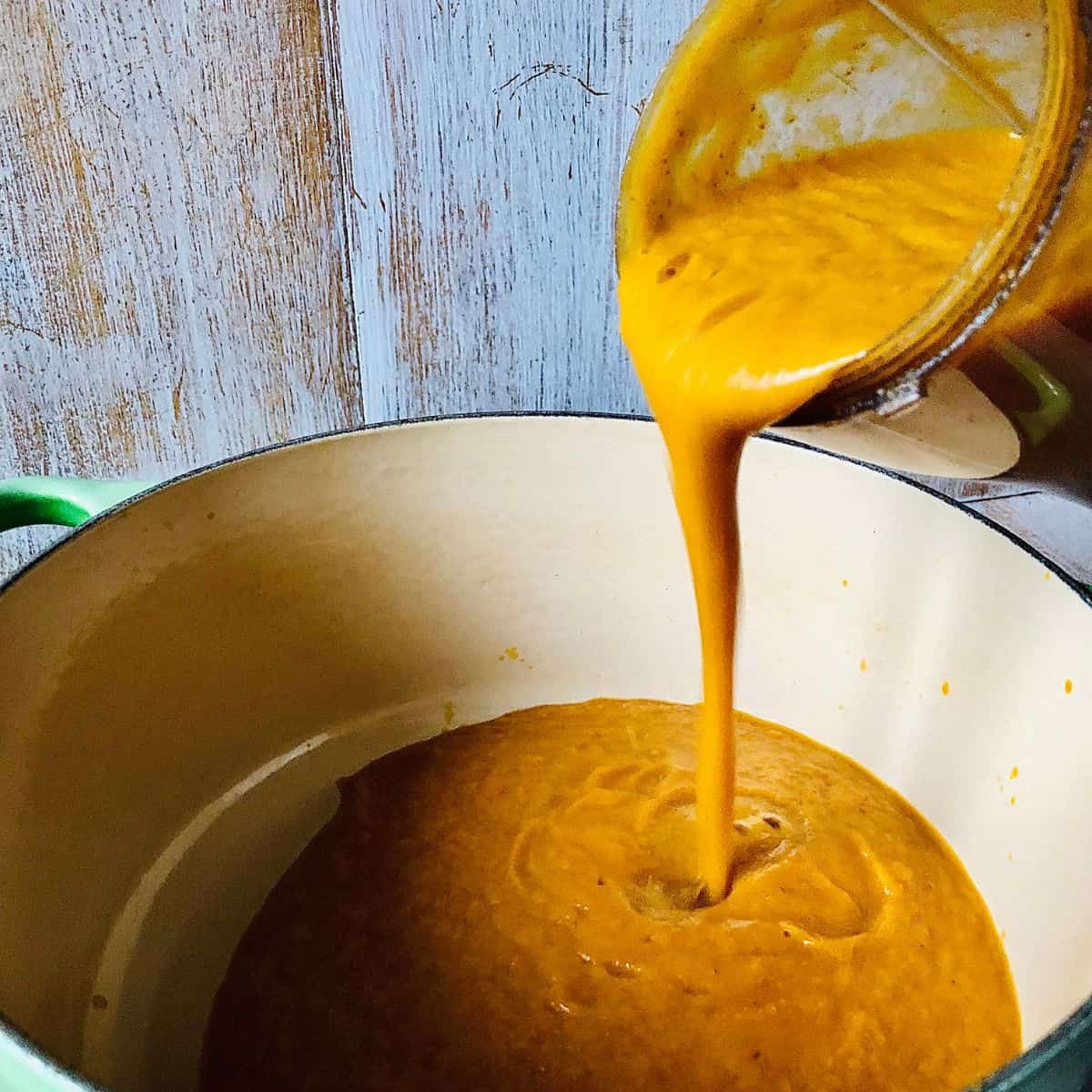 Pouring pureed pumpkin soup from a blender cup into a large pot.