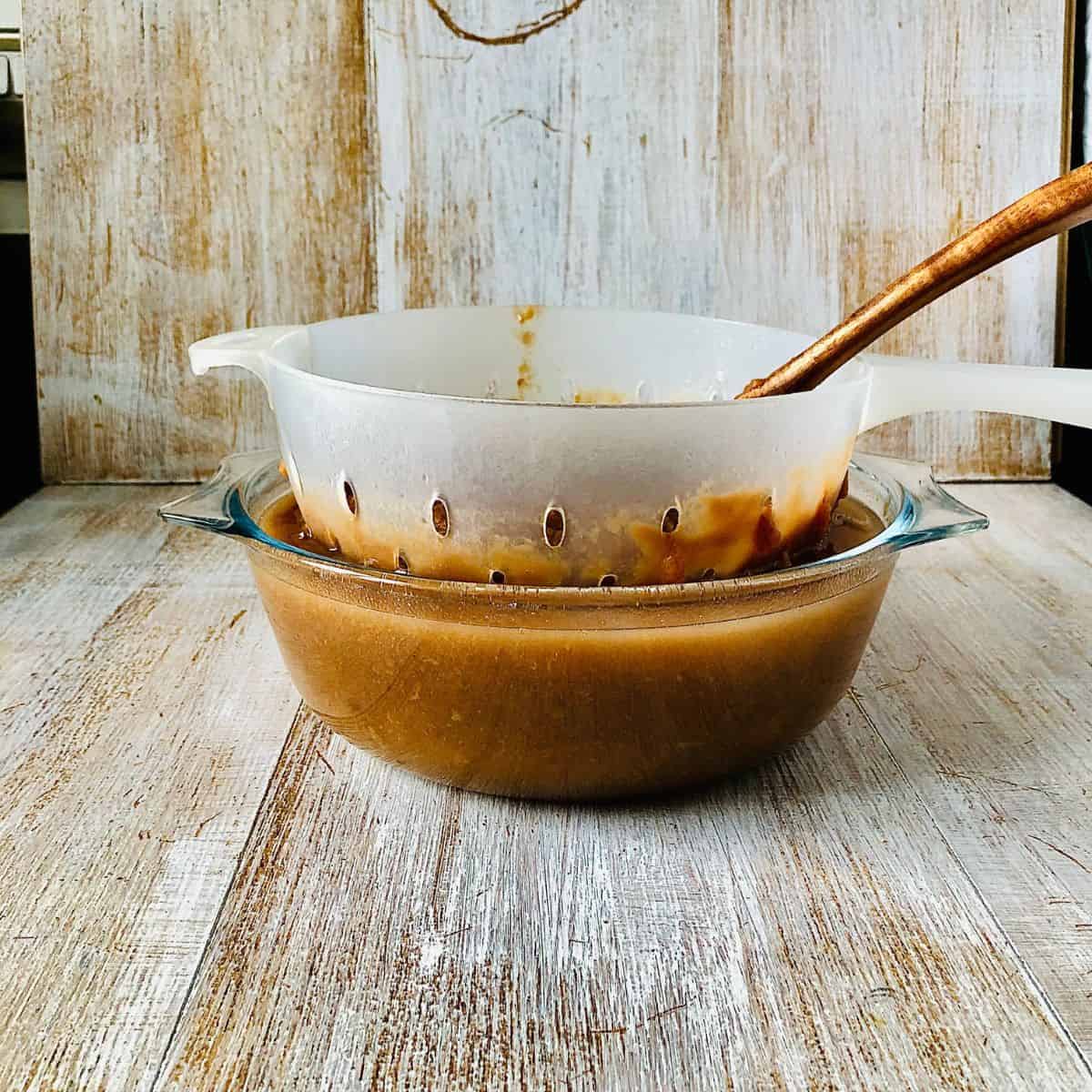 Straining medlar fruit through a colander sitting inside a large glass bowl.