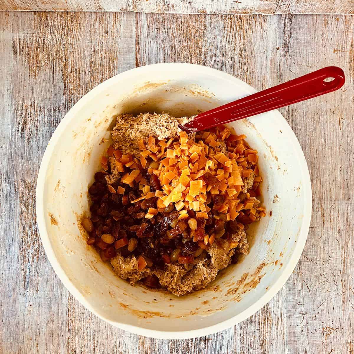 Vegan Christmas cake dough mix in a bowl with chopped alcohol-soaked dried fruit and chopped candied orange added, ready to mix.