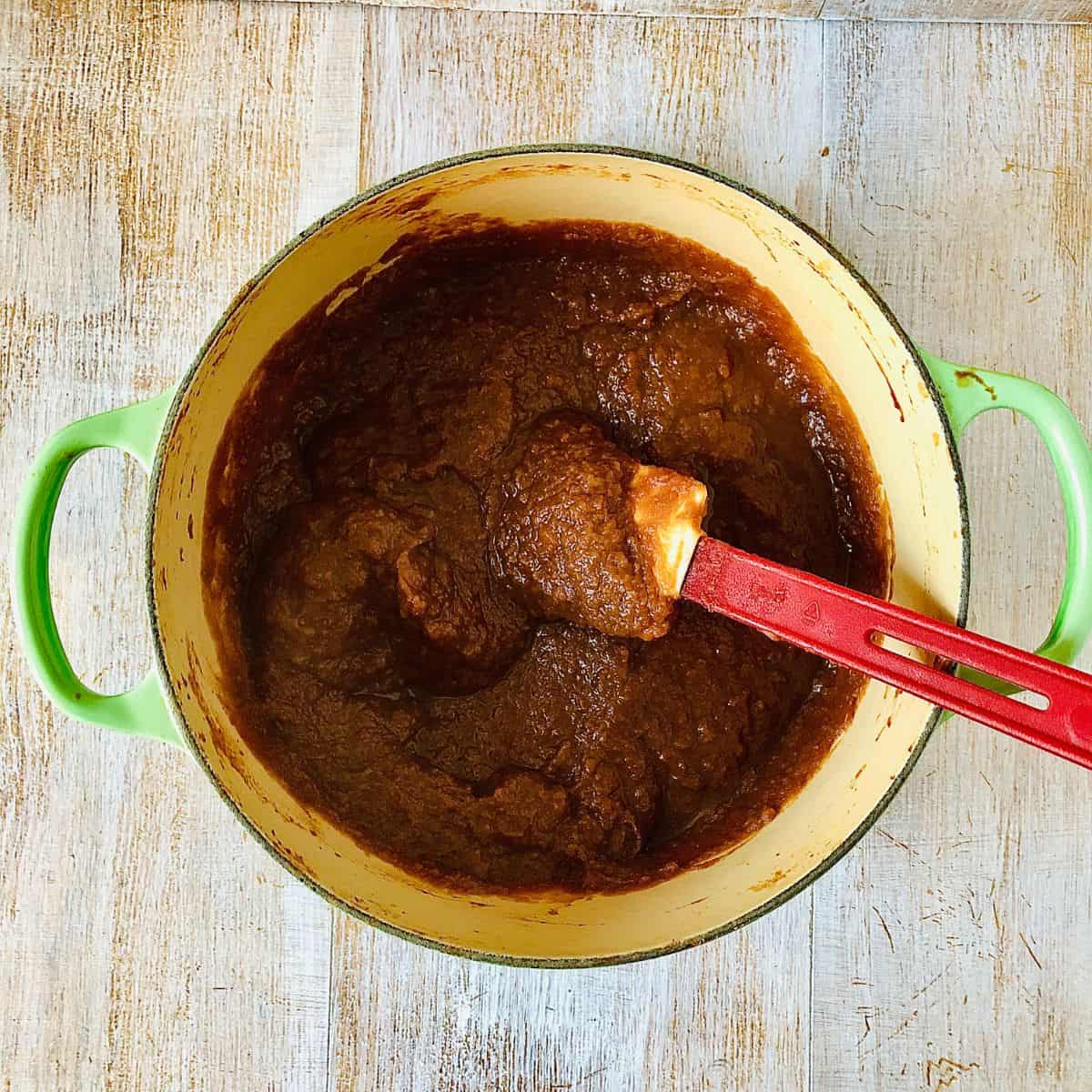 A large pot containing cooked medlar butter with a spatula.