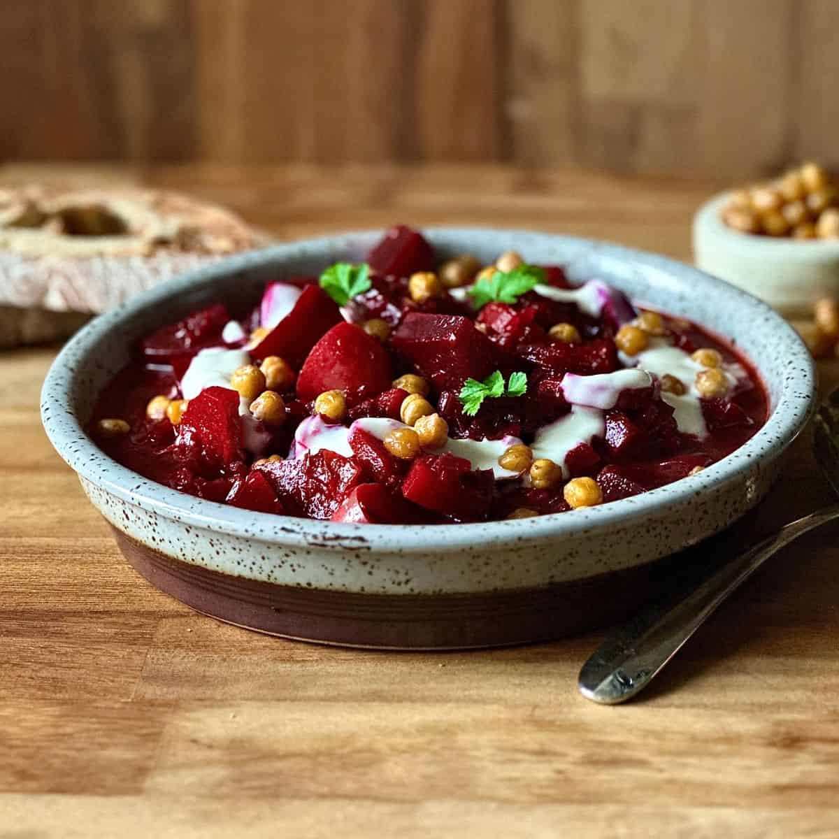 A shallow dish containing beetroot and harissa stew with a yoghurt and chickpea garnish.