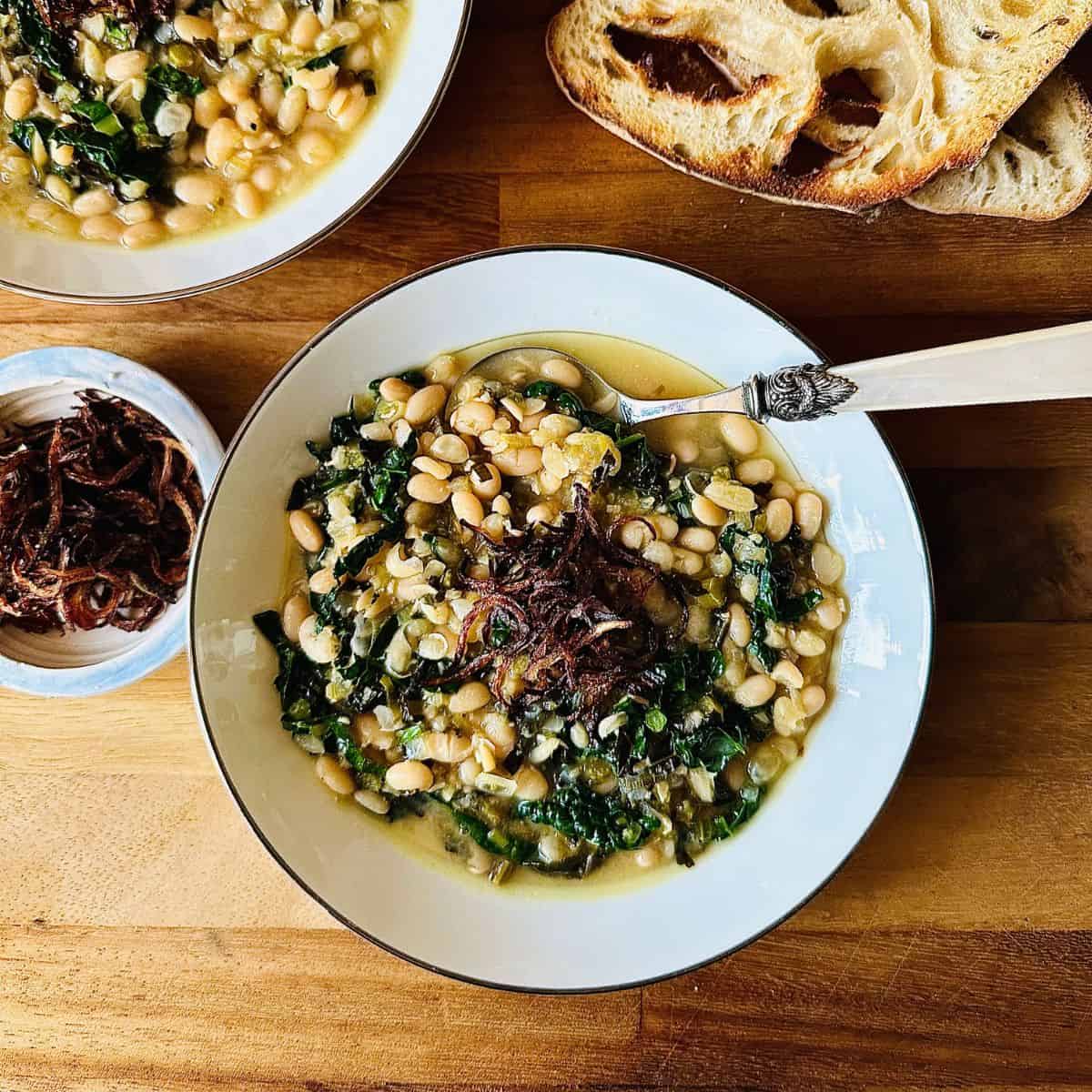 A serving bowl containing haricot bean stew, cavolo nero and a crispy fried onion garnish.