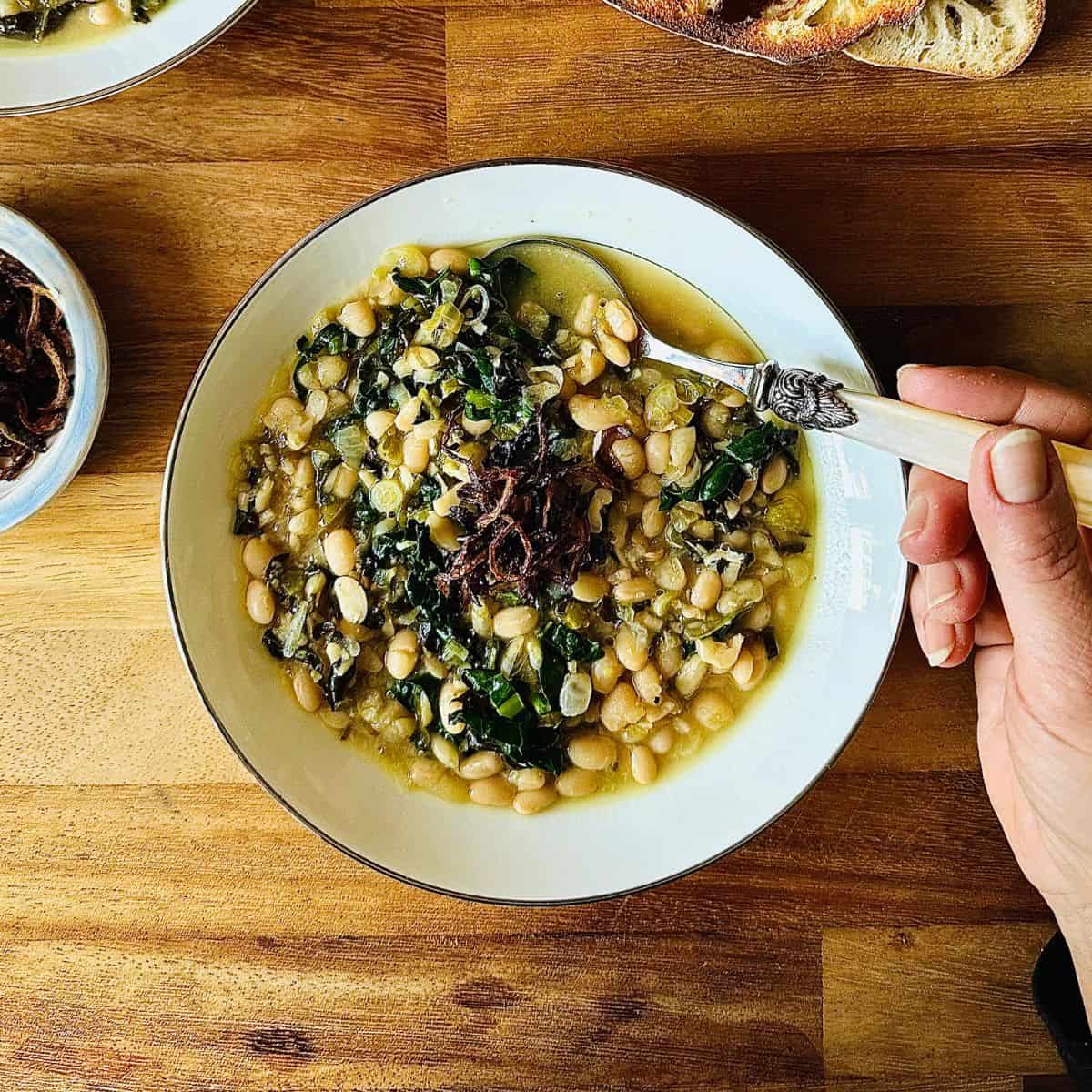 A serving bowl containing haricot bean stew with cavalo nero, and a fried onion garnish.