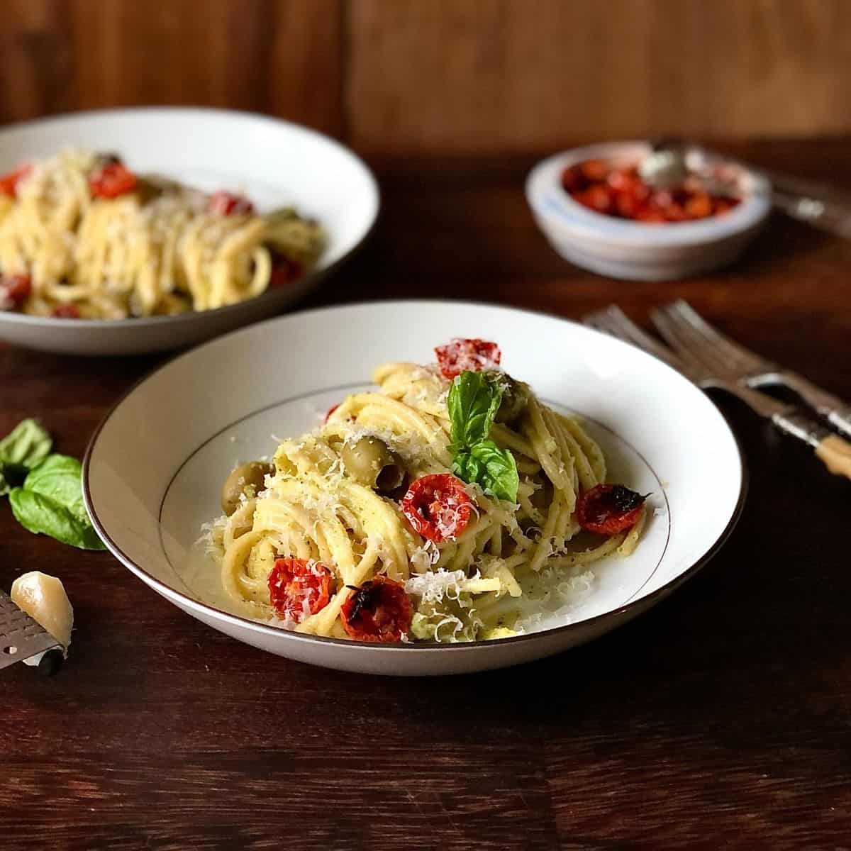 A bowl of spaghetti pasta in a courgette pasta sauce with roasted cherry tomatoes and olives.