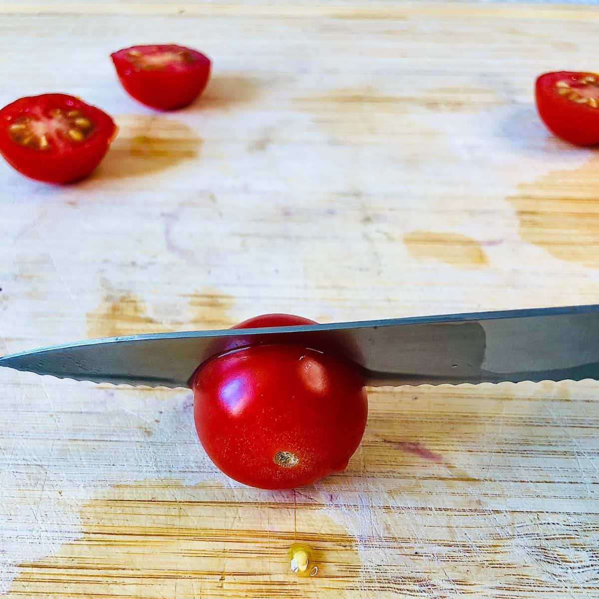 A kitchen knife slicing a cherry tomato in half.