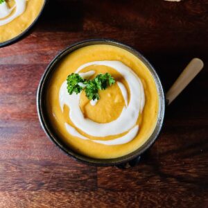 A serving bowl containing winter vegetable soup garnished with vegan yoghurt and a sprig of parsley.