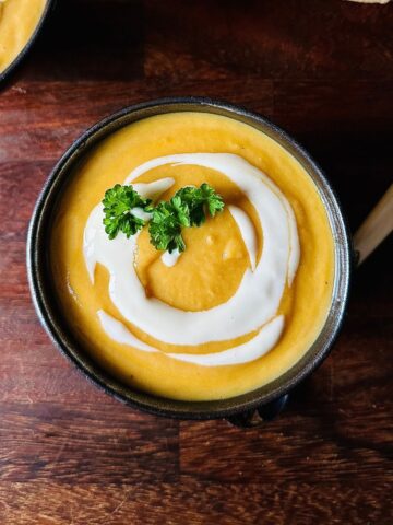 A serving bowl containing winter vegetable soup garnished with vegan yoghurt and a sprig of parsley.