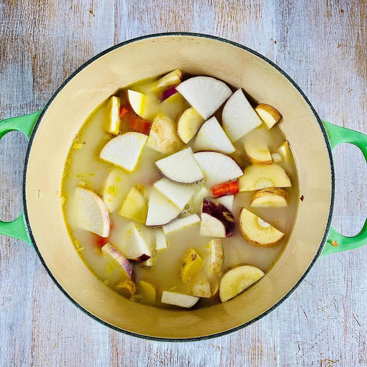 A large pot containing chopped vegetables, vegetable stock and plant milk for winter vegetable soup before blending.