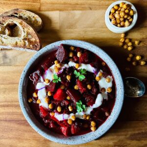 Beetroot and harissa stew in a shallow dish garnished with yoghurt and crispy chickpeas.