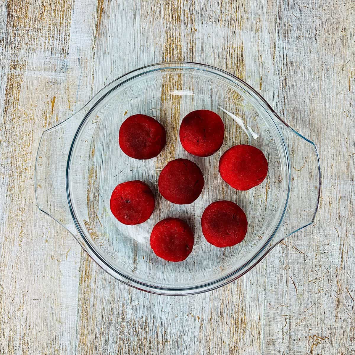 A glass bowl containing seven deep-red coloured mini beetroot burgers ready for frying.