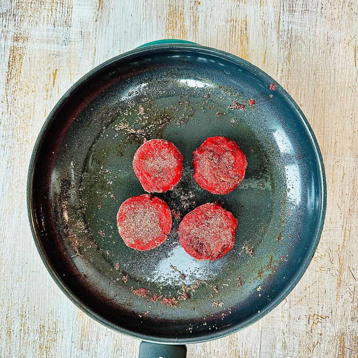 Four mini beetroot burgers frying in a large frying pan.
