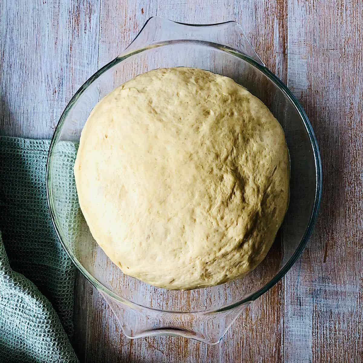 A dough ball for brioche buns in a glass dish after proving and doubling in size.