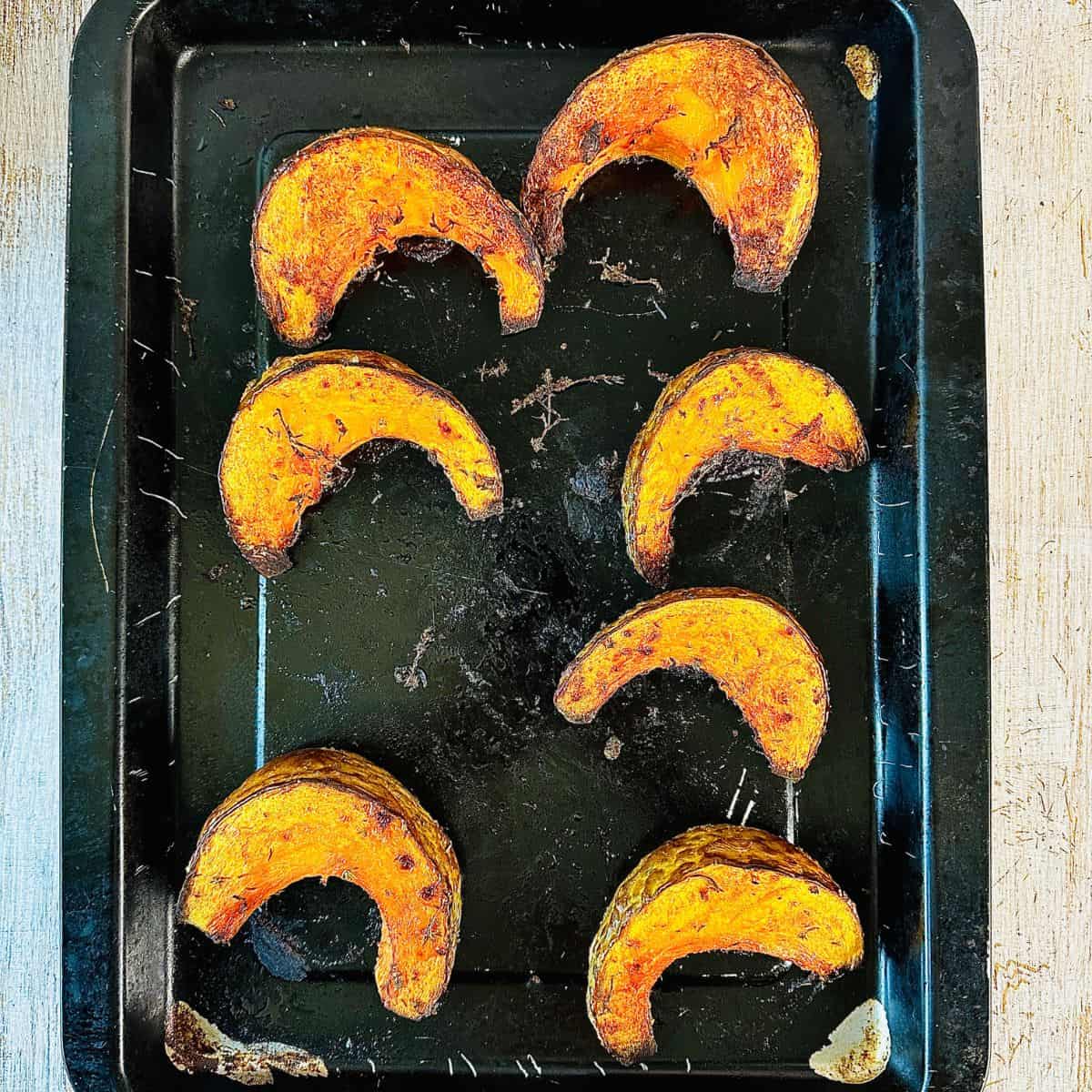 A baking tray/sheet pan with six pumpkin wedges after roasting.