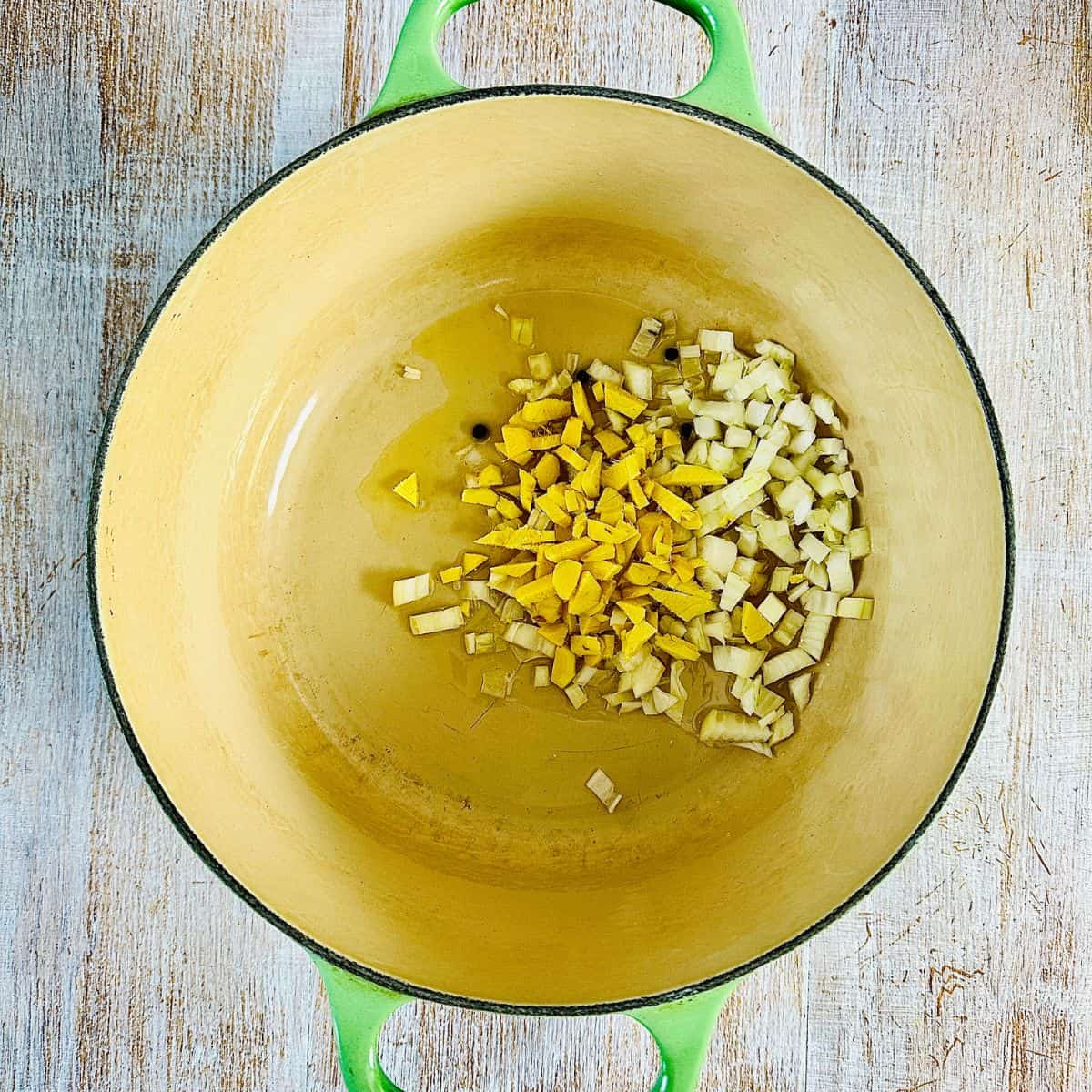 A large pot containing roughly chopped ginger, white onion and peppercorns, frying.