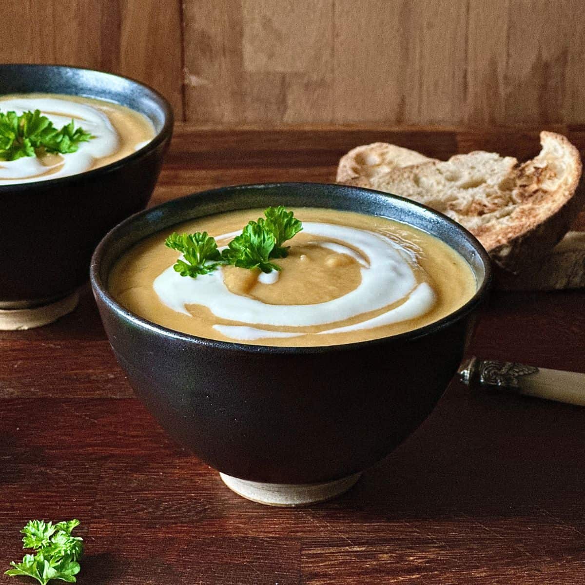 A serving bowl containing winter vegetable soup garnished with vegan yoghurt and a sprig of parsley.