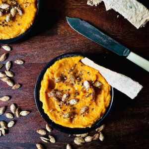 Pumpkin dip garnished with pumpkin seeds in a small black dish.
