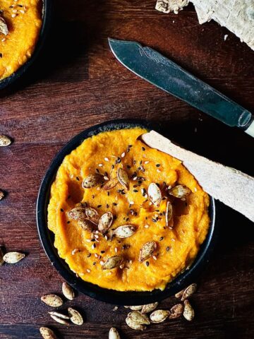 Pumpkin dip garnished with pumpkin seeds in a small black dish.