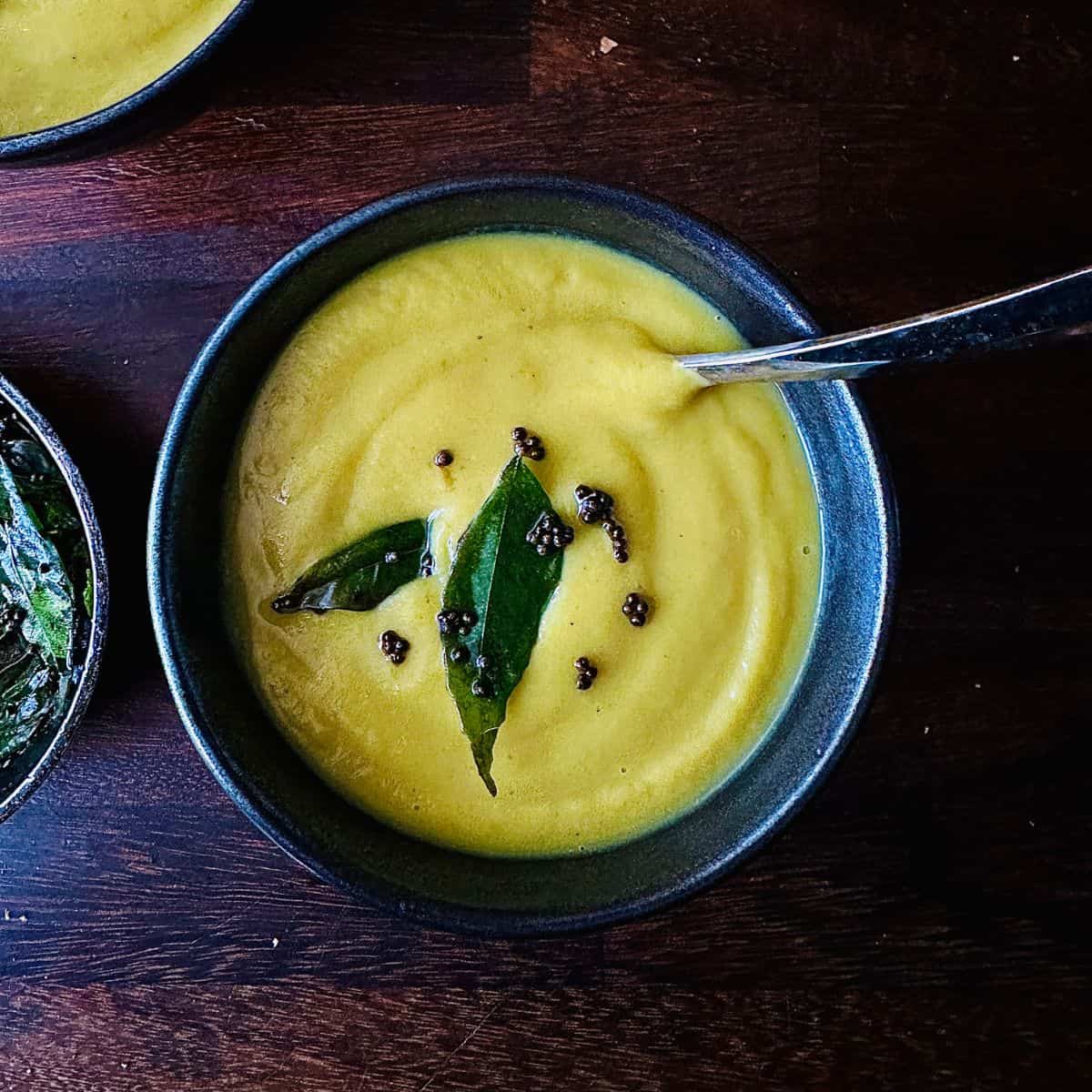 A serving bowl containing curried parsnip soup with a curry leaf and mustard seed garnish.
