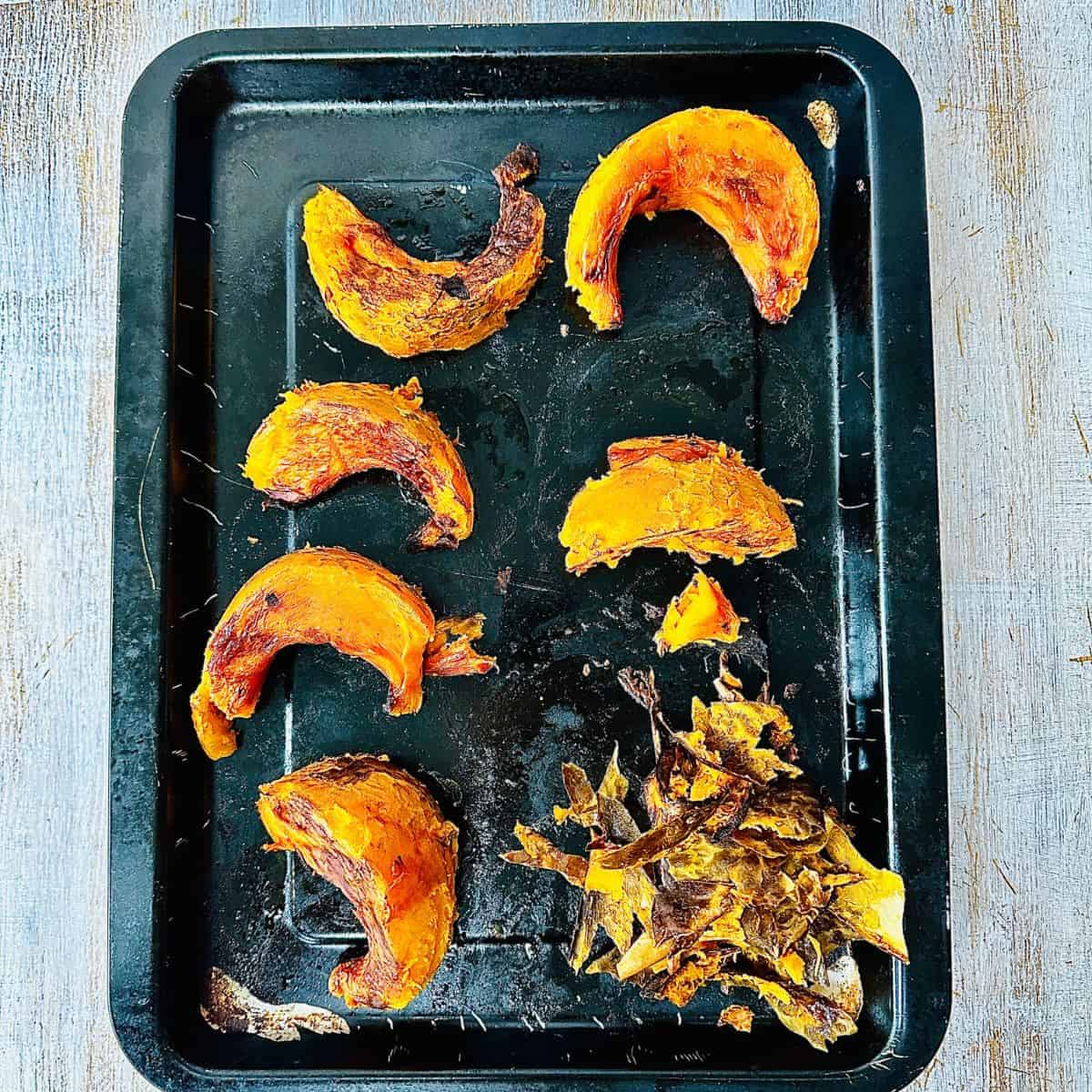 A baking tray containing roasted pumpkin wedges with skin removed. The skin is piled in one corner of the baking tray.