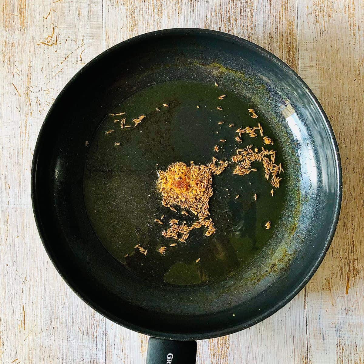 Asafoetida and cumin seeds frying in a pan.