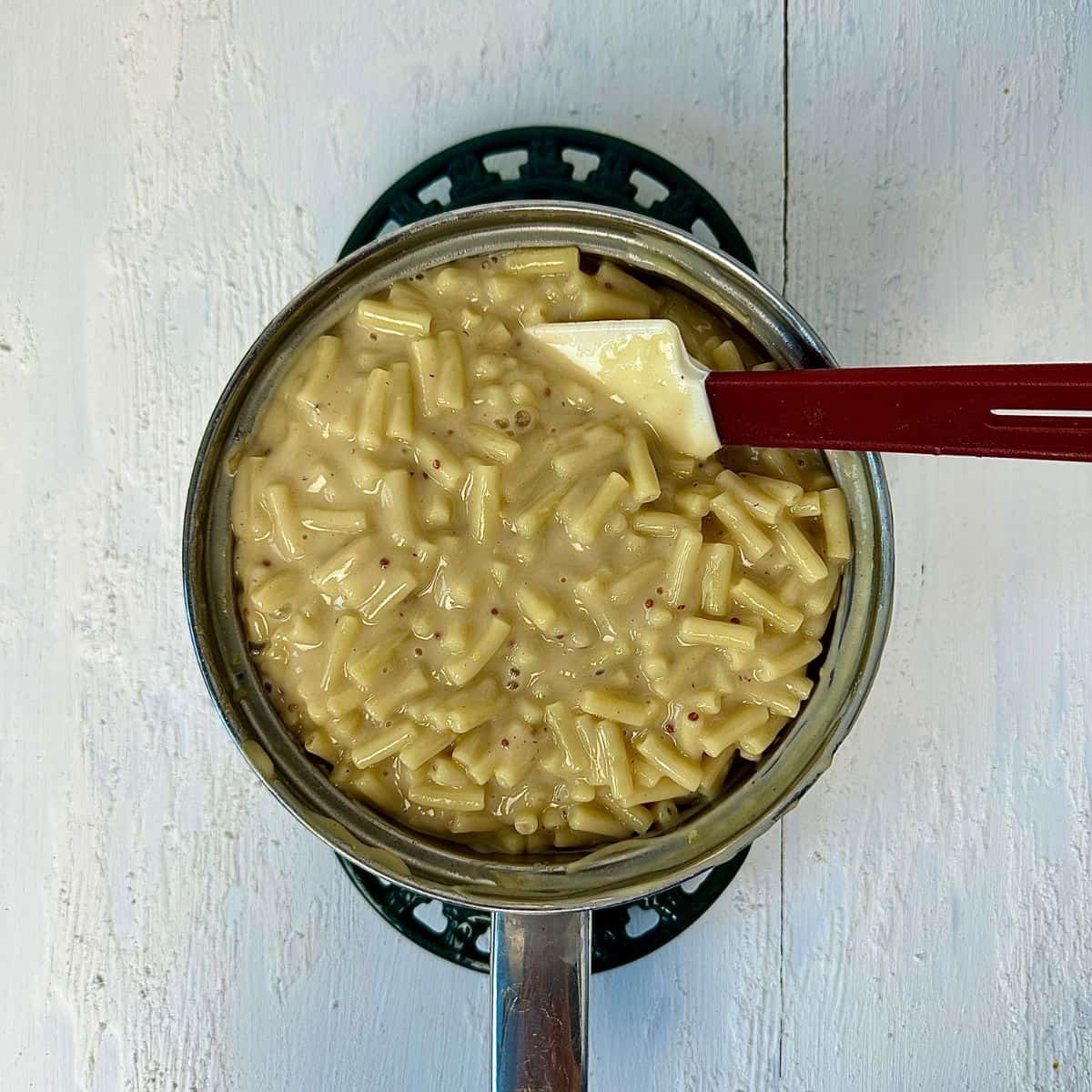 A stainless steel saucepan containing cooked macaroni mixed with a vegan cheese sauce.
