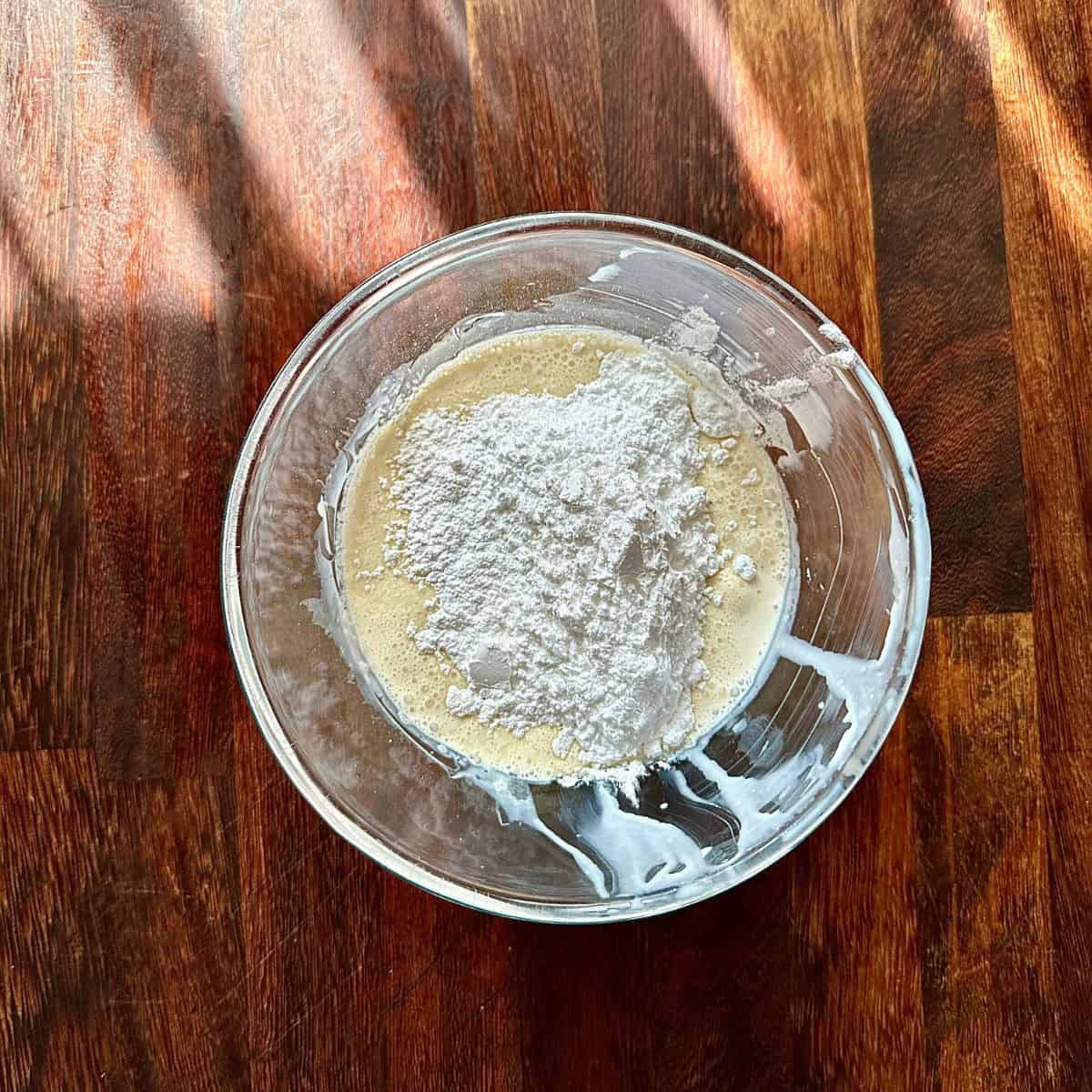 A glass bowl containing whipping cream infused with elderflower and icing sugar, ready to mix.