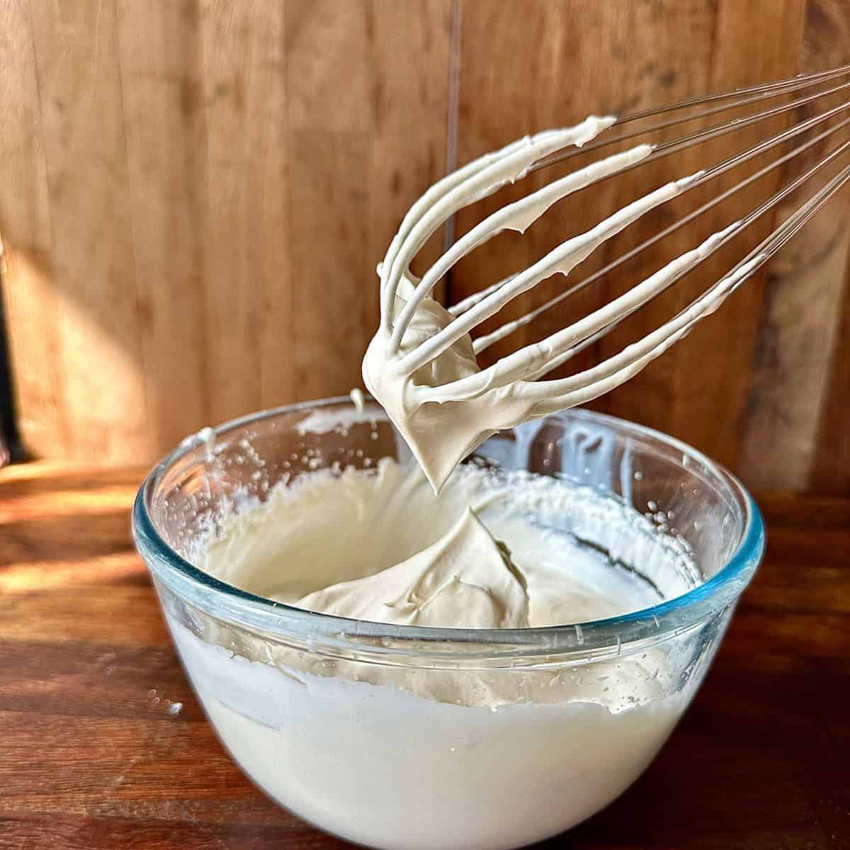 A glass bowl containing whipped vegan cream in soft peaks.