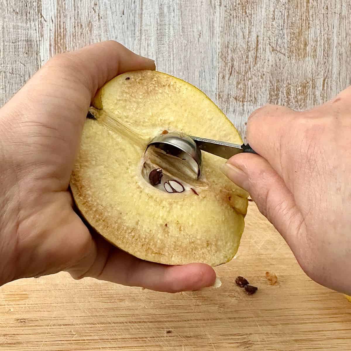 Close up of scooping out the core and seeds of a halved quince using a small scooping tool.