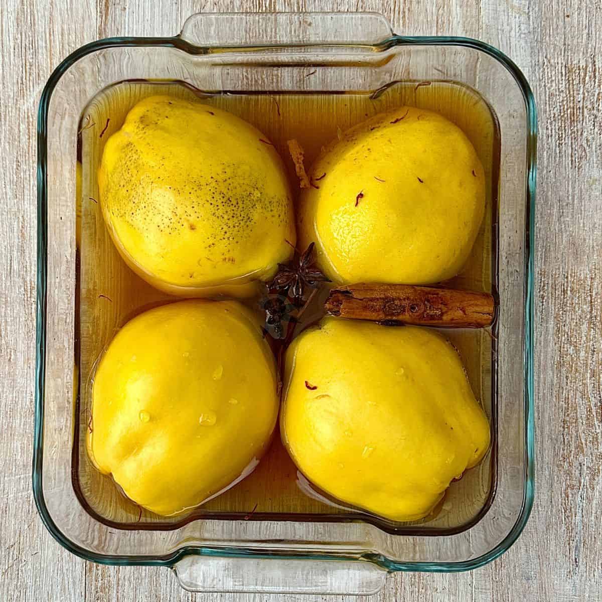 A glass oven dish containing four Quince halves sitting in a liquor ready for baking.