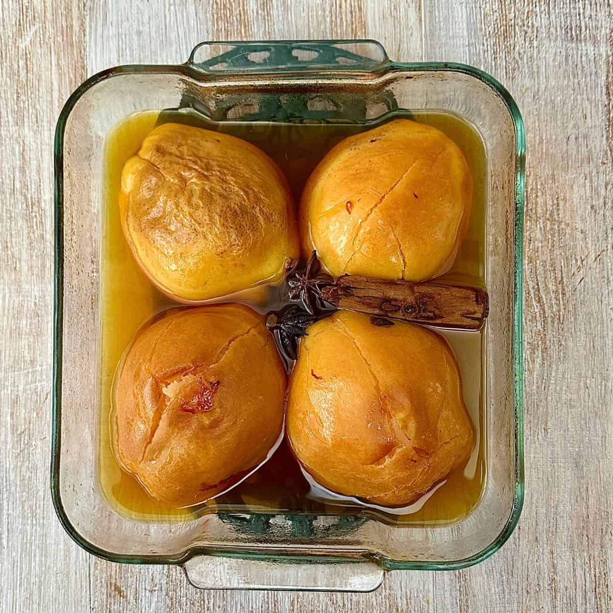 A glass oven dish containing four Quince halves sitting in a liquor after one hour of baking.