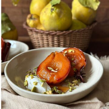 Baked quince with a serving of cream cheese and sprinkled with pistachios in a small, shallow beige bowl.