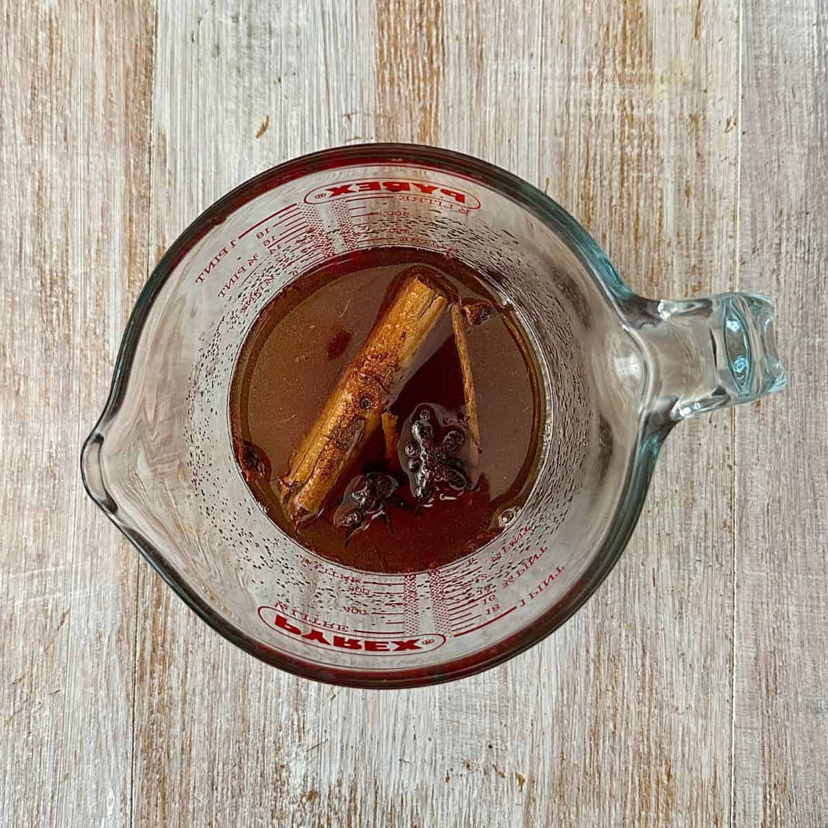 A glass measuring jug containing the ingredients for the liquor for the baked Quince recipe.