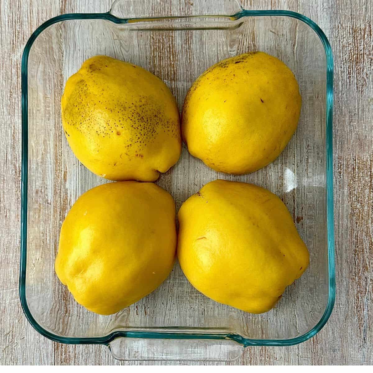 A glass oven dish contain four Quince halves, face down, ready to bake.
