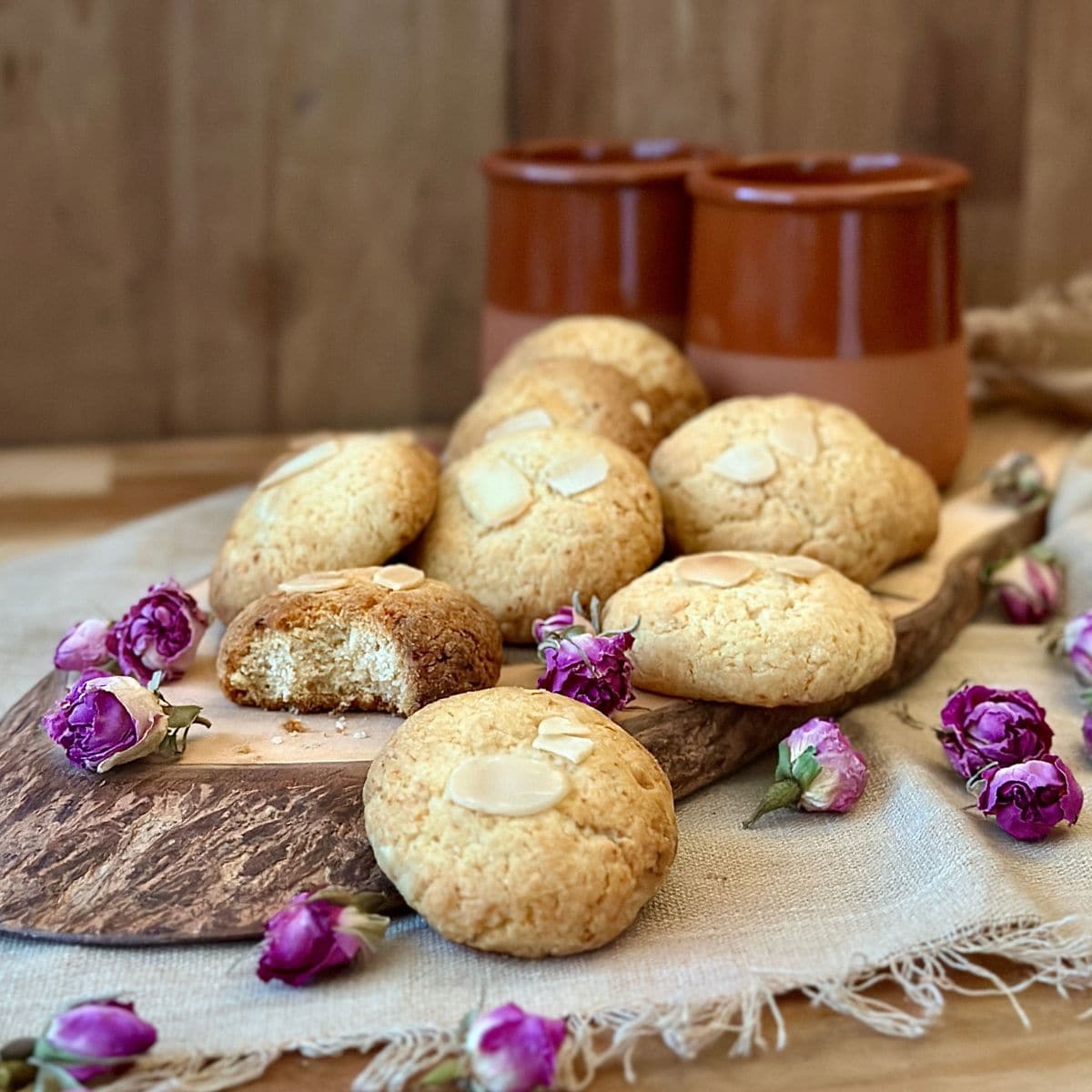 Gulab Jamun cookies on a sliced tree-trunk platter with purple rose buds scattered around for decoration. Two ceramic cups sit in the background.