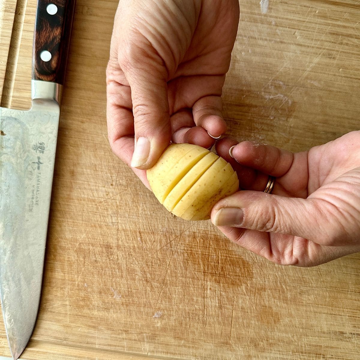 Close up of hands holding a baby potato cut hasselback-style showing the knife cuts.