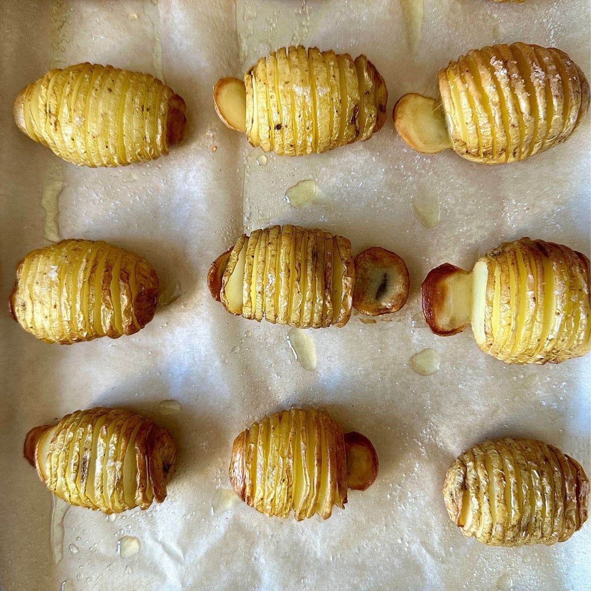 Nine Hasselback baby potatoes on a parchment paper-lined baking tray after baking.