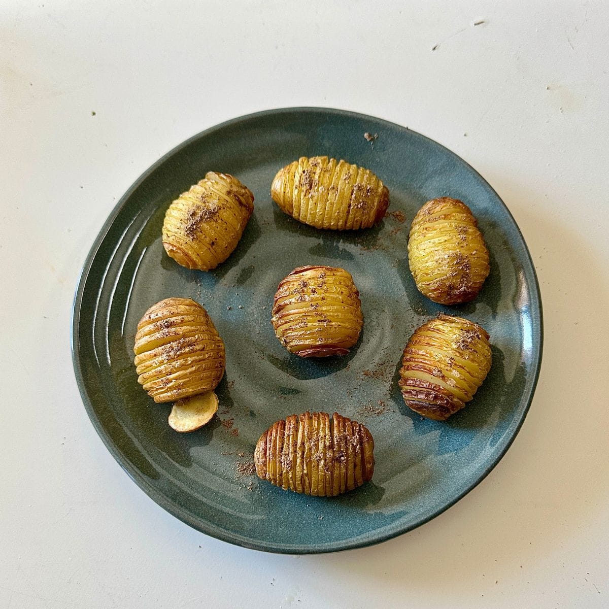 Seven cooked hasselback potatoes sprinkled with chaat masala, arranged on a serving palate.