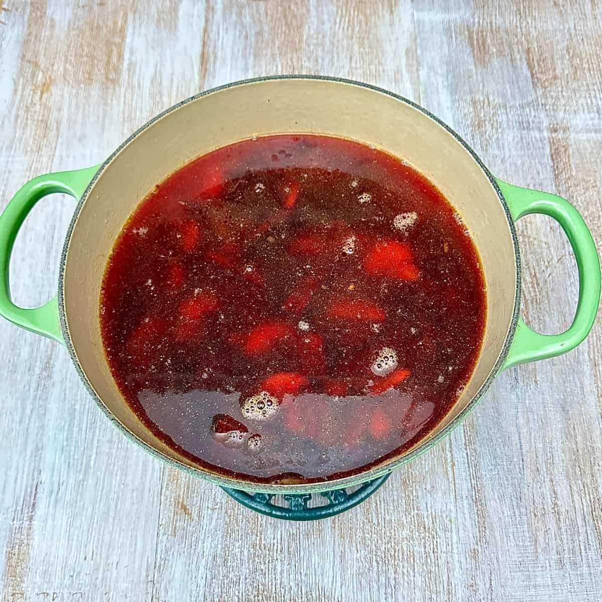 A large green pot containing beetroot, carrot, onion, garlic and vegetable stock ready to cook.
