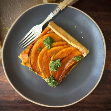 A square slice of crown prince pumpkin galette with rocket pesto on a small round serving plate.