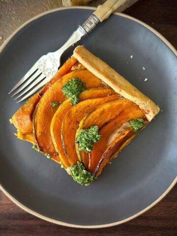A square slice of crown prince pumpkin galette with rocket pesto on a small round serving plate.