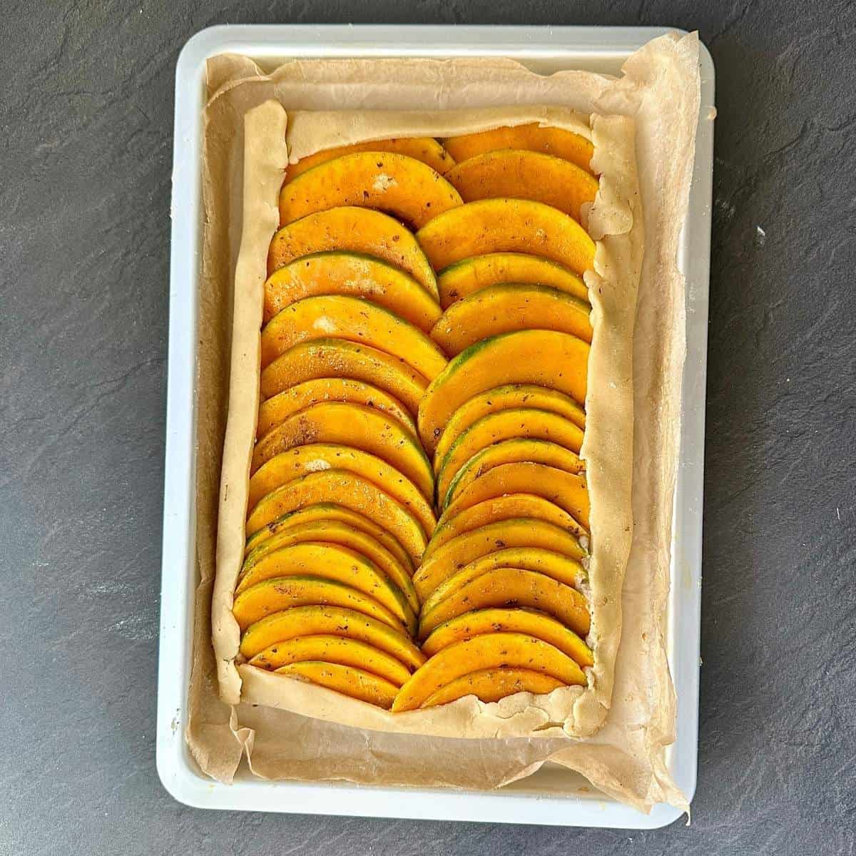 A pumpkin galette in a baking tray ready for baking sat upon parchment paper.
