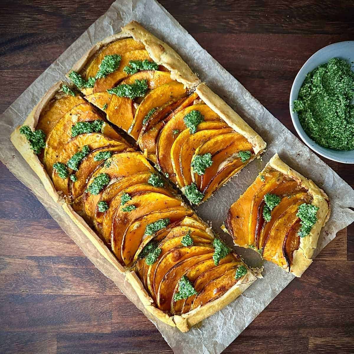 Six portions of pumpkin galette with wild rocket pesto sitting on parchment paper and wooden chopping board.