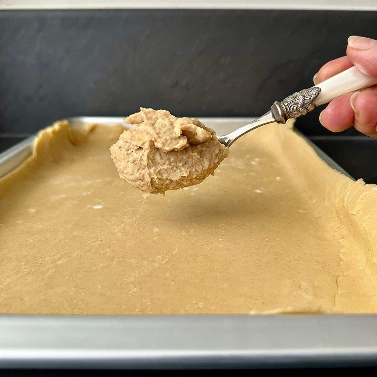 Close up of a spoon containing butterbean puree help over a baking tray containing pastry for a pumpkin galette.