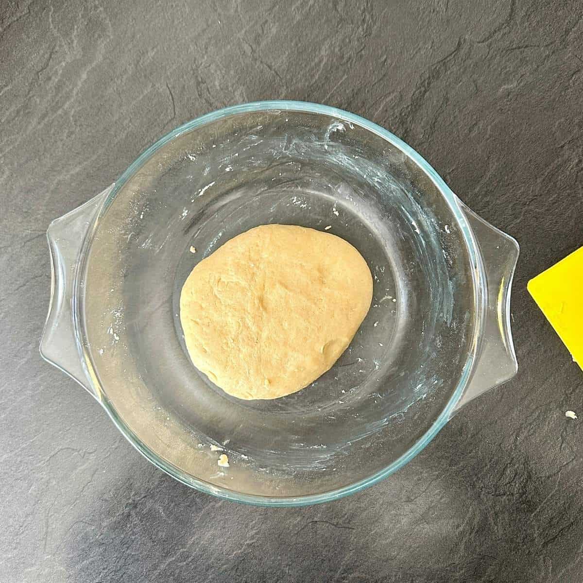 A glass bowl containing dough flattened to a disk shape.