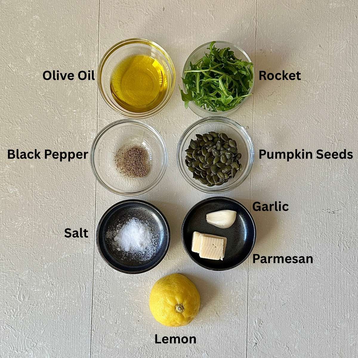 Ingredients for rocket pesto in small glass and ceramic dishes.