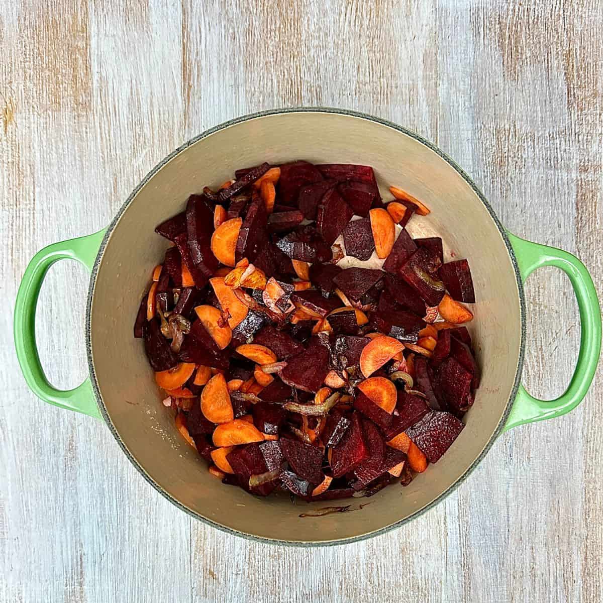 A large green pot containing sliced carrot and beetroot ready to cook for beetroot soup.