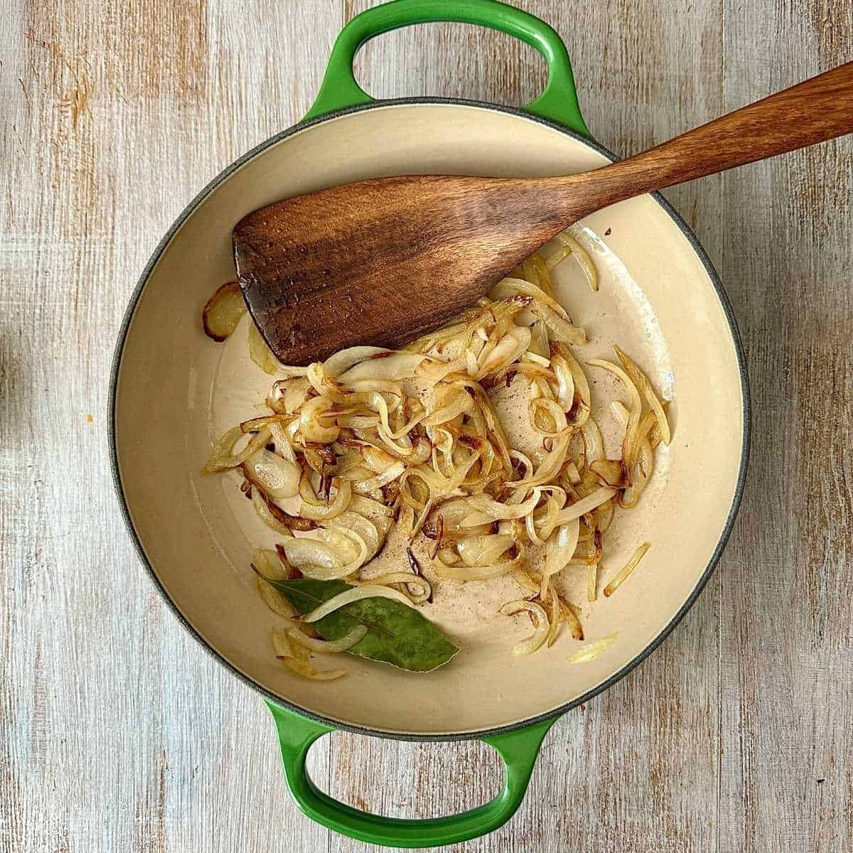 A large green ceramic pot containing caramelised onion and a bay leaf after cooking.
